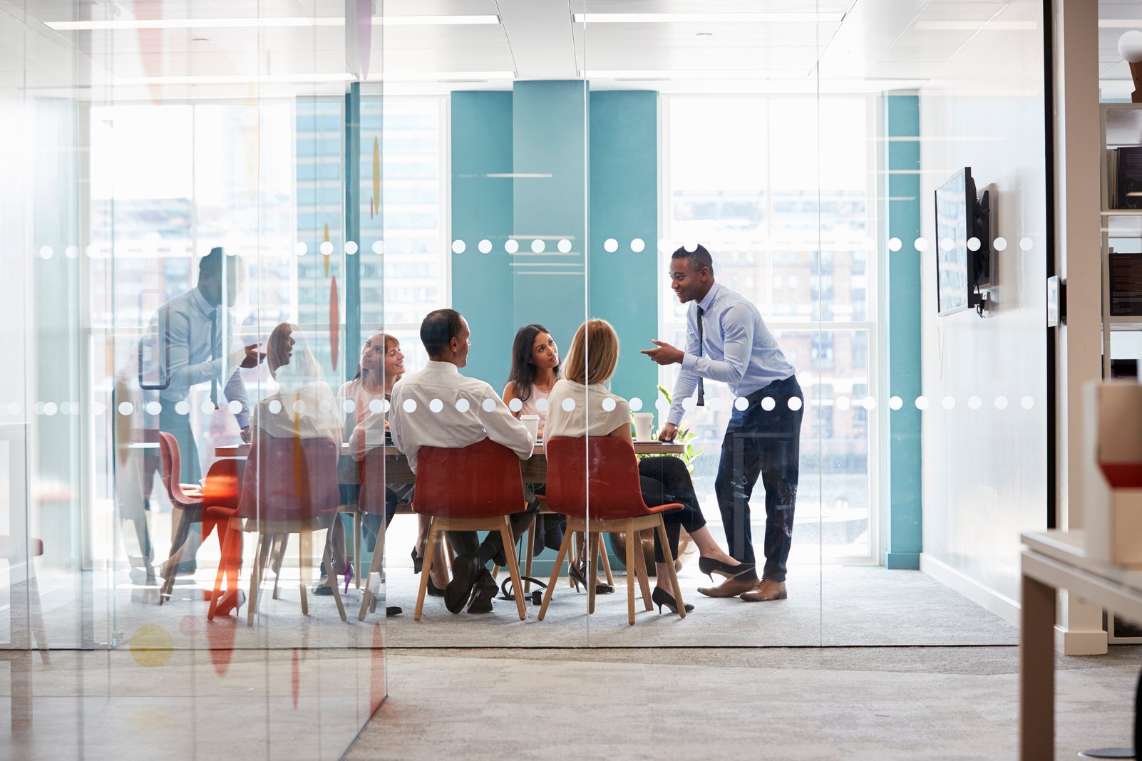 Young Male Boss Stands Leaning on Table at Business Meeting